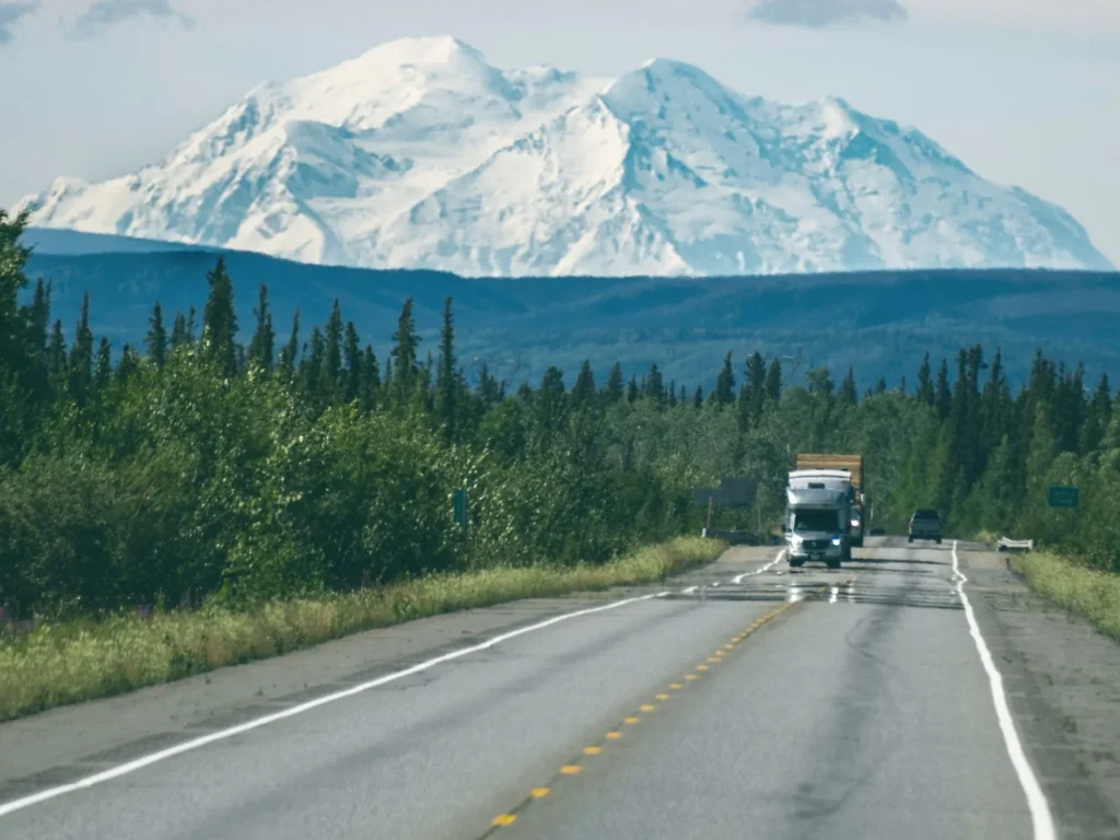 Camión de carga solo en una carretera recta, con una montaña nevada al fondo