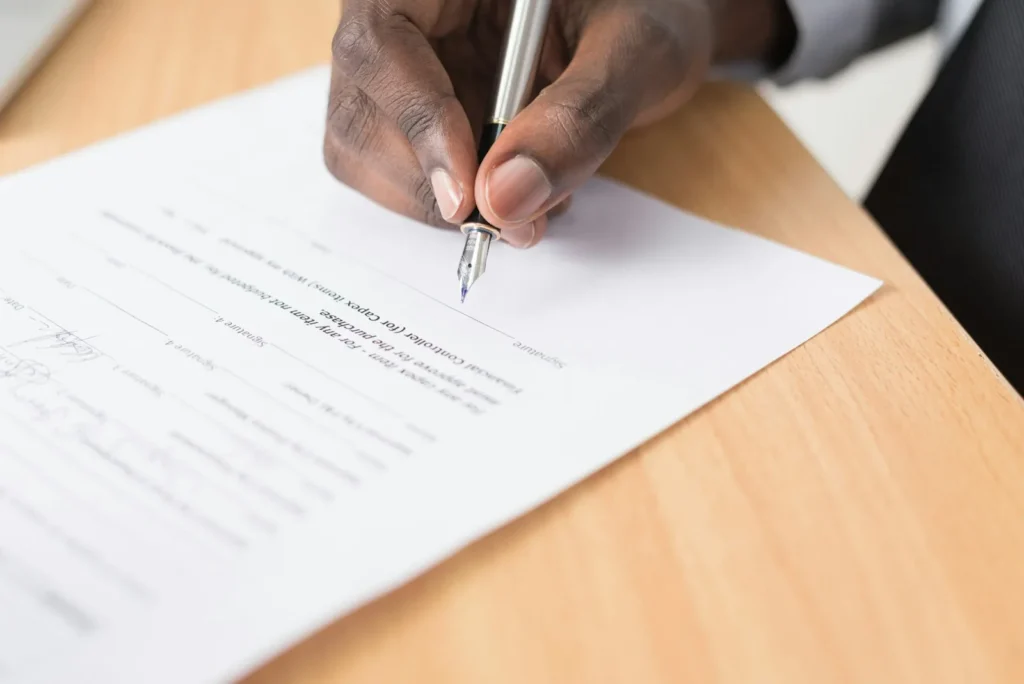 Una mano firma un formulario impreso apoyado en un escritorio
